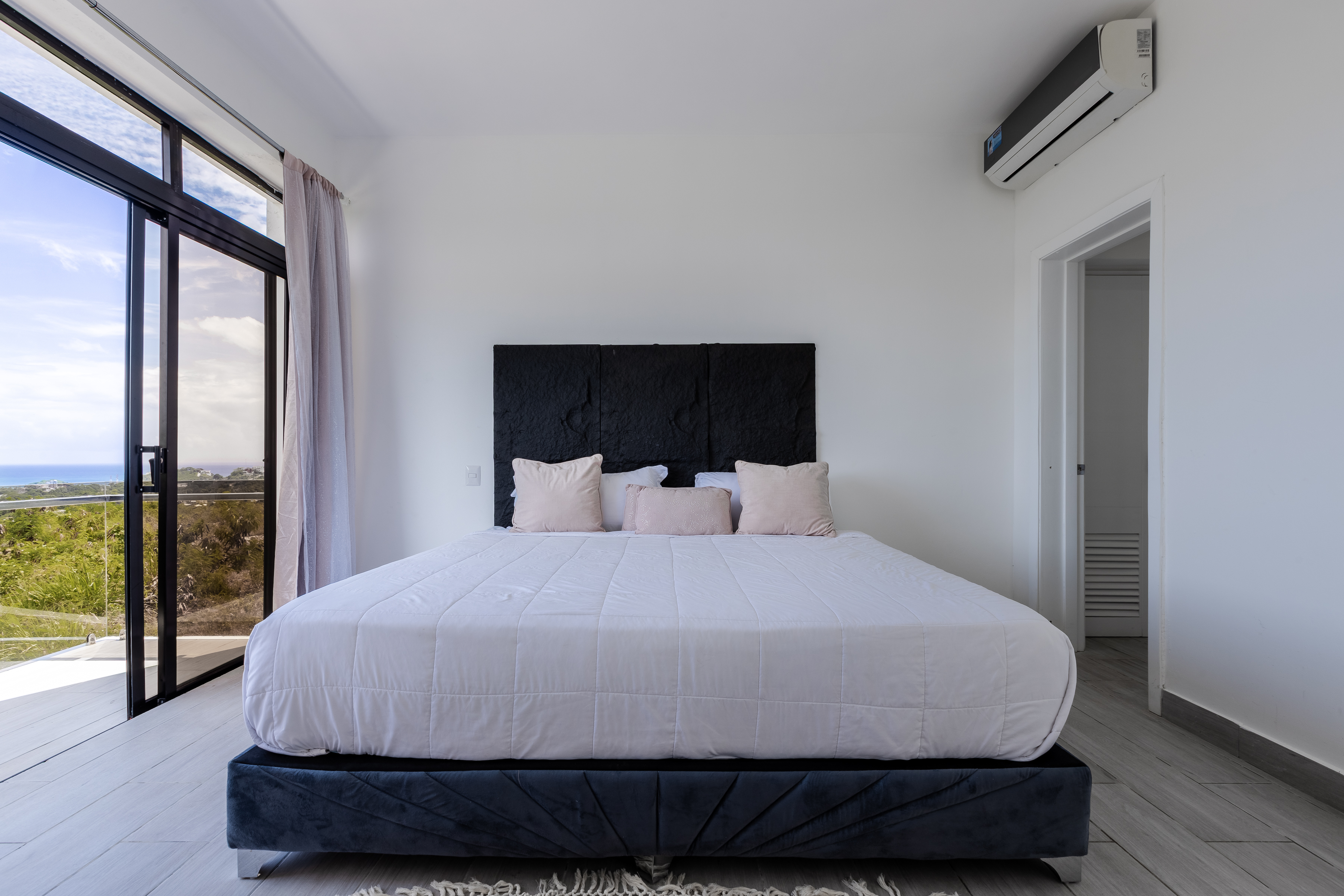 Clean white bedroom with glass door opening to the Caribbean